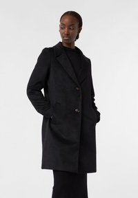 Cappotto in misto lana nero con colletto a scollo a V, due tasche frontali e chiusura a tre bottoni. Texture liscia e vestibilità aderente.