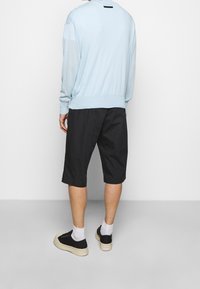 Maglione azzurro chiaro e pantaloni corti neri. Il maglione ha un collo a giro e polsini a coste; i pantaloni sono lunghi fino al ginocchio. Sneakers nere con suole bianche.