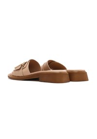 Tan leather slip-on shoes with a thick, textured sole, featuring a rounded shape and a decorative metallic accent on the upper.