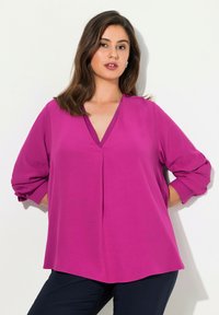 Blusa fucsia a scollo a V con maniche a tre quarti, in tessuto morbido e vestibilità comoda. Caratterizzata da dettagli plissettati e polsini con bottoni.