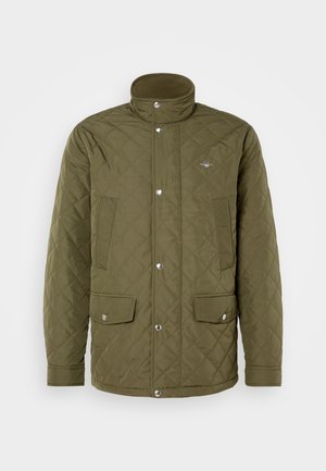 Olíva zöld steppelt dzseki magas gallérral, patentgombokkal és két elülső zsebbel. Az anyag sima textúrájú, gyémánt mintázatú varrással.