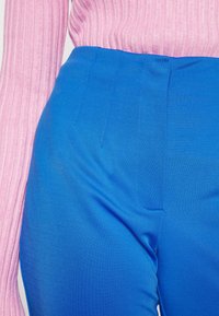 Gros plan d'une personne portant un pantalon taille haute bleu vif et un haut côtelé rose à manches longues rentré.