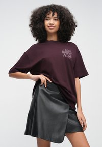 T-shirt oversized bordeaux com um design gráfico subtil no peito, combinada com uma saia curta de couro preta, com uma fenda frontal.