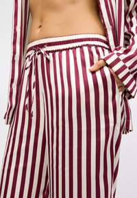 Pajama set s črtastim vzorcem s tankimi maroon in krem črtami; material se zdi gladek in mehak; elastični pas z vrvico; gumbne podrobnosti.