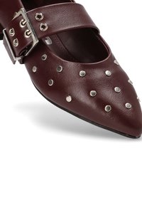 Zapato de cuero burdeos con punta afilada, adornado con tachuelas plateadas y una correa ancha que presenta una gran hebilla plateada.