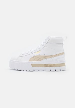 Biały, wysokogatunkowy sneaker Puma z beżowym paskiem po boku, grubą białą podeszwą, złotym logo Puma i sznurowanym zapięciem.