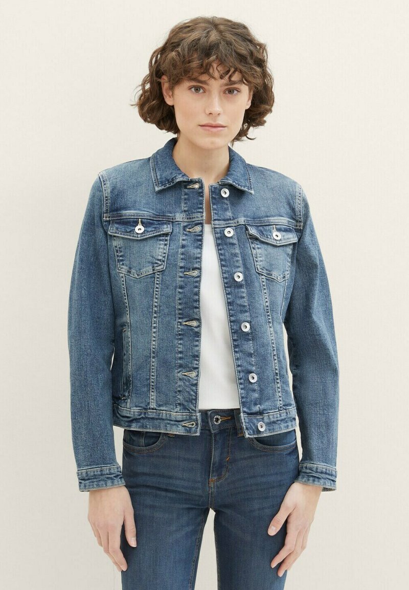 Giacca di jeans blu medio con colletto, bottoni frontali, due tasche sul petto e maniche lunghe. Presenta un design aderente e linee pulite.