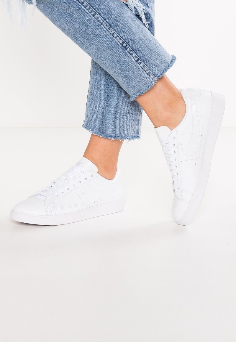 Zapatillas deportivas blancas con parte superior de cuero liso, punta redonda y suela de goma plana. Presentan un diseño con cordones y un mínimo de marcas.