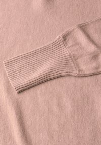 Hellrosa Pullover mit einer glatten Textur, der ein geripptes Bündchen hat. Der Stoff hat ein weiches, feines Strickbild.