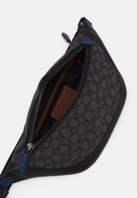 Sac en cuir noir et toile enduite avec un motif circulaire gris, fermeture éclair, accents bleus et intérieur marron avec une étiquette.