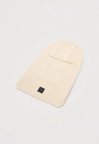 Bonnet en tricot crème avec une texture côtelée, présentant un revers et une petite étiquette carrée noire sur le côté.