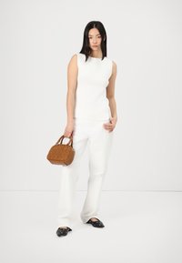 Haut sans manches blanc à côtes, pantalon large blanc, ballerines noires pointues avec œillets en argent, et un petit sac à main en cuir texturé marron.