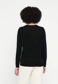 Čierny sveter s dlhými rukávmi a okrúhlym výstrihom s jemnou textúrou. Jednoduchý dizajn s rebrovanými manžetami a lemom, doplnený svetlo béžovými nohavicami.