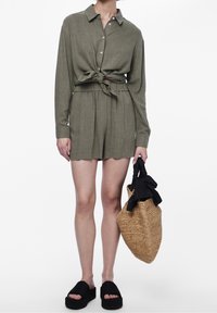 Oliivinvihreä pellavapaita solmittavalla edellä, yhdistettynä samanvärisiin shortseihin. Mustat tasapohjasandaalit ja punottu olkilaukku täydentävät asun.