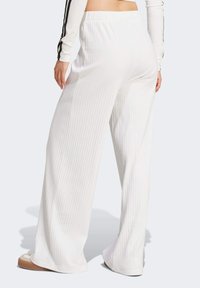 Vita vida byxor med ribbad textur, utrustade med ett elastiskt midjeband och subtila skuggningar längs benen, kombinerat med lätta skor.