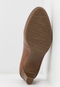 Suola di scarpa in pelle marrone con fondo in gomma testurizzata, caratterizzata da scanalature orizzontali e verticali per una migliore aderenza. Sfondo neutro.