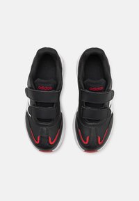 Zapatillas deportivas negras con acentos rojos, fabricadas en material sintético, con una textura suave, dos correas de velcro y una suela blanca.