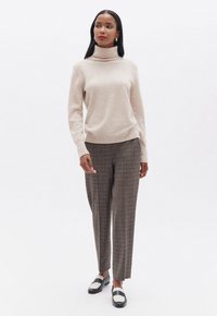 Suéter de cuello alto beige y pantalones de cuadros. El suéter es suave, mientras que los pantalones están ajustados con un patrón en marrón y gris. Mocasines negros con acentos en blanco.