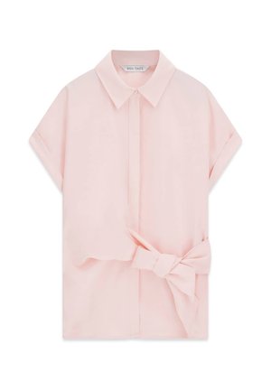 Blouse rose clair à manches courtes avec un col classique et un grand nœud en tissu noué à la taille sur le côté droit.