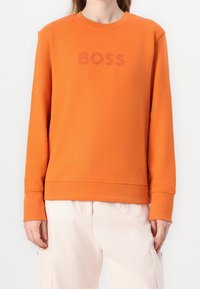 Orange sweatshirt made of cotton, featuring a round neckline and ribbed cuffs. Front displays the text "BOSS" in a slightly darker shade.