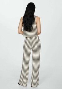 Knitted two-piece outfit featuring a cropped top with vertical stripes and wide-leg pants, both in cream with thin black zigzag patterns.