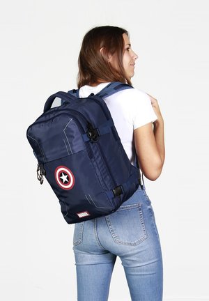 Mochila azul marino con un emblema circular rojo y blanco, diseño elegante, correas resistentes y acentos reflectantes; fabricada con material duradero.