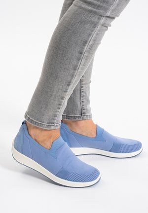 Blaue Slipper aus einem gemischten Obermaterial mit strukturierten Akzenten und einer weißen Gummisohle. Getragen mit grauen, enganliegenden Jeans.