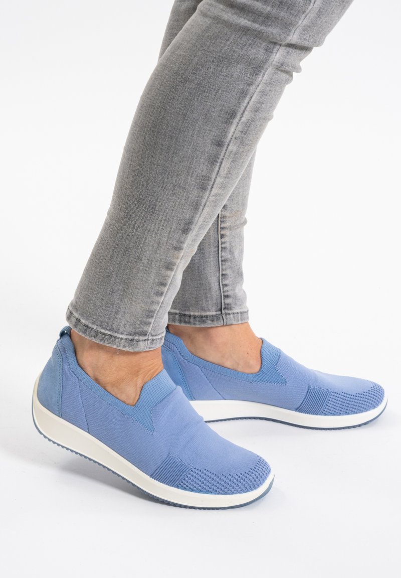 Modré slip-on boty s svrchním materiálem z kombinovaných látek, zdobené texturovanými prvky a bílou gumovou podrážkou. Nosené s šedými úzkými džíny.