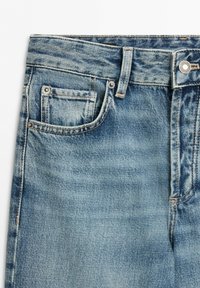 Close-up of light blue denim jeans showing front pocket, small coin pocket, belt loops, button, and zipper fly area.