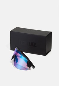 Lunettes de soleil avec une monture noire et une grande lentille irisée montrant des nuances de rose et de bleu. Accompagnées d'une boîte rectangulaire noire.