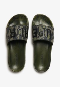 Groene camouflageslippers met een brede zwarte band waarop "SUPERDRY" in vette letters staat. Glad, textuur bovenwerk en een gevoerde groene zool.
