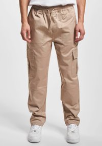 Beige cargo-housut, joissa on joustava vyötärö, useita taskuja ja suora lahjetekstuurimuoto. Materiaalit näyttävät sileiltä ja kevyiltä.