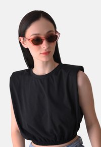 Top nero corto con orlo arricciato e design senza maniche, abbinato a occhiali da sole a forma di occhio di gatto con tonalità rosa. Tessuto dalla consistenza liscia.