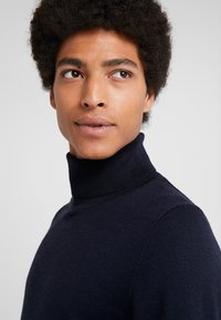 Donkerblauwe turtleneck trui van gebreide stof met een gladde textuur en een aansluitend ontwerp, voorzien van geribbelde accenten bij de kraag.