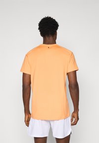 Kurzärmliges, orangefarbenes T-Shirt mit Rundhalsausschnitt, glatter Textur und einem kleinen schwarzen Detail an der Schulter, kombiniert mit einer weißen Shorts.