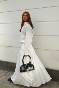 White shirt and flowing white skirt, paired with a small black leather handbag. The outfit features a clean design and lightweight fabric.