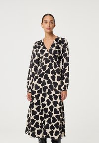 Zwart-crème jurk met lange mouwen, voorzien van een hartjesprint, V-hals en een taillebanddetail, gemaakt van lichtgewicht stof.