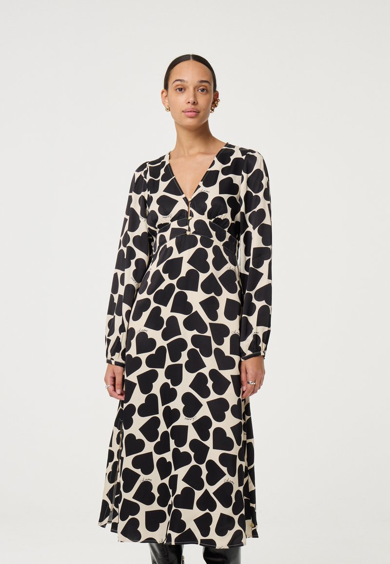 Zwart-crème jurk met lange mouwen, voorzien van een hartjesprint, V-hals en een taillebanddetail, gemaakt van lichtgewicht stof.