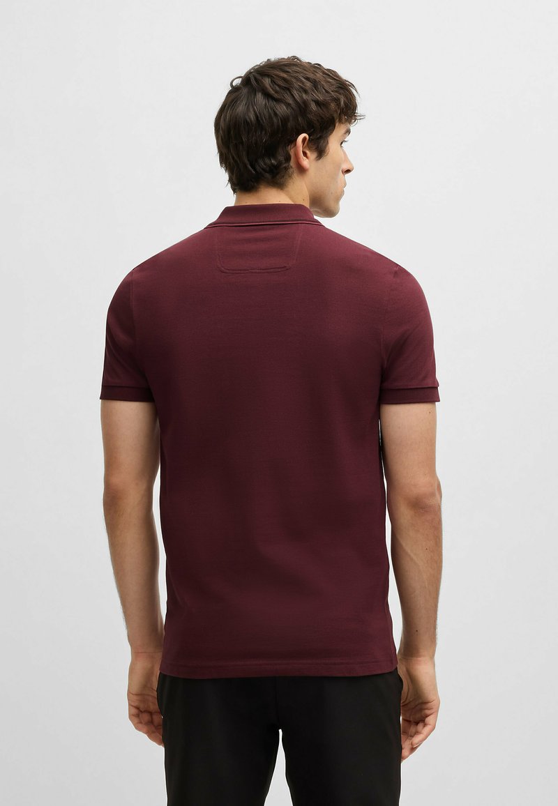 Bordeaux kortemouw polo met een klassieke kraag, een gladde brei structuur en een subtiele achterkant label detail.