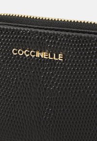 Black textured wallet with a zip closure and gold-tone "Coccinelle" logo. The surface features a raised pattern, adding dimension.
