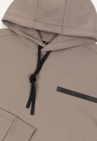 Taupefarbener Hoodie mit schwarzen Kordeln und dem Schriftzug "Coular Originals" auf der Brust.