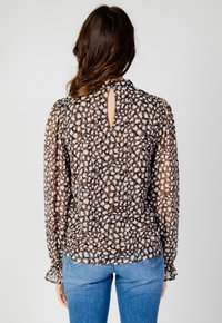 Blusa a righe marroni e bianche con schiena a chiave, maniche lunghe e scollatura leggermente arricciata. Indossata con jeans blu.