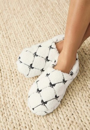 Valged karvased sisetallad mustade lipsumustritega, millel on pehme ja tekstureeritud välimus. Ümar kuju, avatud tagaosa ja pehme sisu.