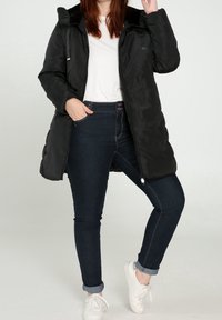 Musta untuvatakki hupulla, jossa on sileä pinta, vetoketju- ja napeilla suljettava malli, yhdistetty tummiin farkkuihin ja valkoisiin lenkkareihin.