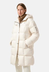 Padded cream-colored coat with a hood, featuring a zip front, two side pockets, and elasticized cuffs. Textured, warm knit collar.