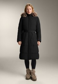 Cămașă neagră căptușită cu guler înalt și glugă căptușită cu blană, talie cu curea și mâneci lungi. Purtați peste colanți negri și cizme căptușite cu blană.