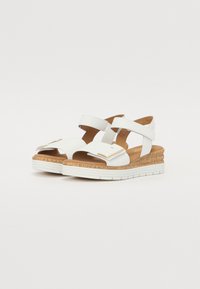 White leather wedge sandals with two wide straps, cork midsole, and a textured white sole. Features a gold accent on the front strap.