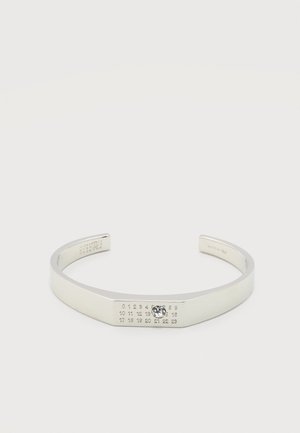 Bracelet manchette en argent ouvert avec les chiffres gravés de 0 à 23 et une petite pierre précieuse claire sertie au numéro 14 sur un fond blanc.