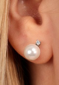 Orecchini rotondi con perle in montatura argentata, caratterizzati da un'accattivante accentatura di diamante sopra la perla. Texture liscia e lucida di colore bianco.