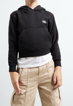 Sudadera negra recortada con bolsillo frontal y parche con logo, combinada con pantalones cargo beige con bolsillos laterales y tejido texturizado.